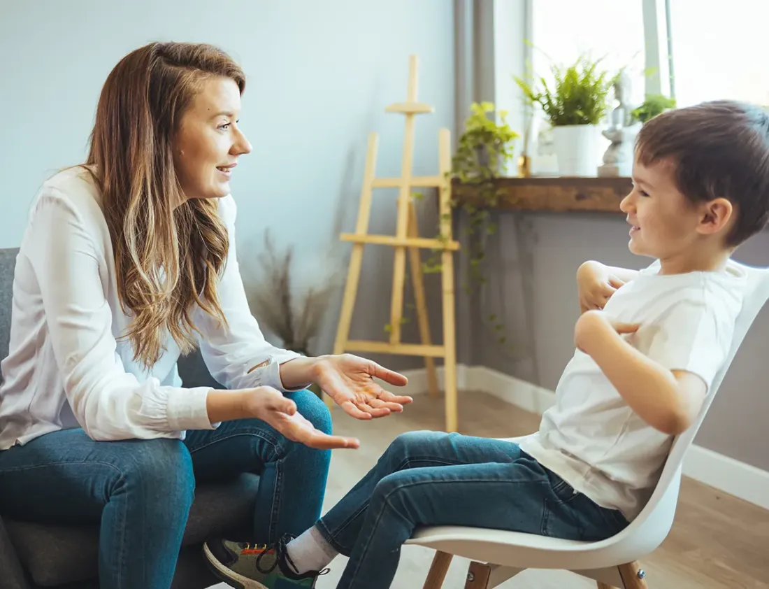 A woman talking with a young boy in a lounge room, gesturing as they chat