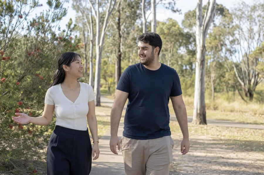 Behaviour support practitioner walking with a young adult participant along a path lined with gum trees in a Parramatta park