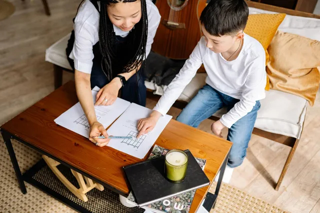 A woman and a boy working together over a sheet of paper at a table