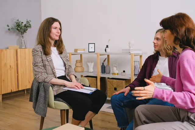 A practitioner with a notepad talking with two clients during a session in a bright room