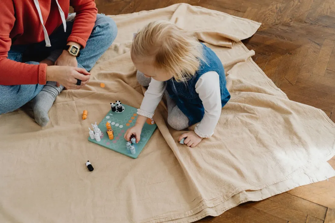 A child and an adult playing a board game together on a blanket on the floor