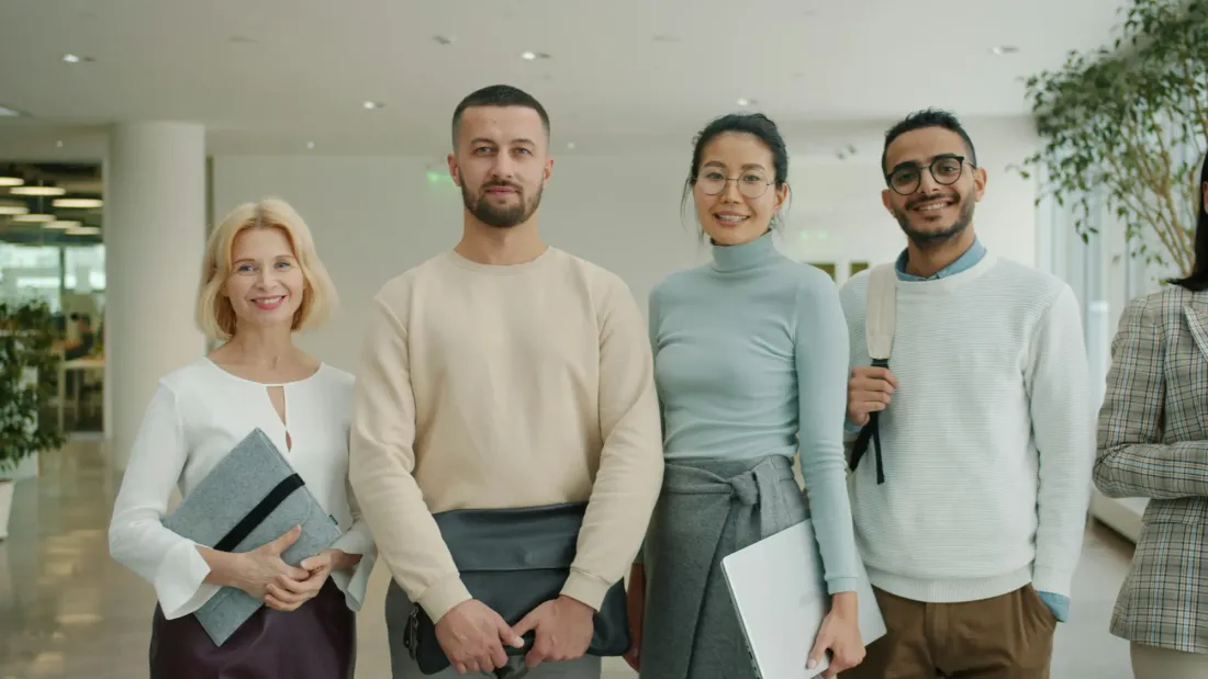 A smiling man and woman standing together in a bright office, with colleagues beside them