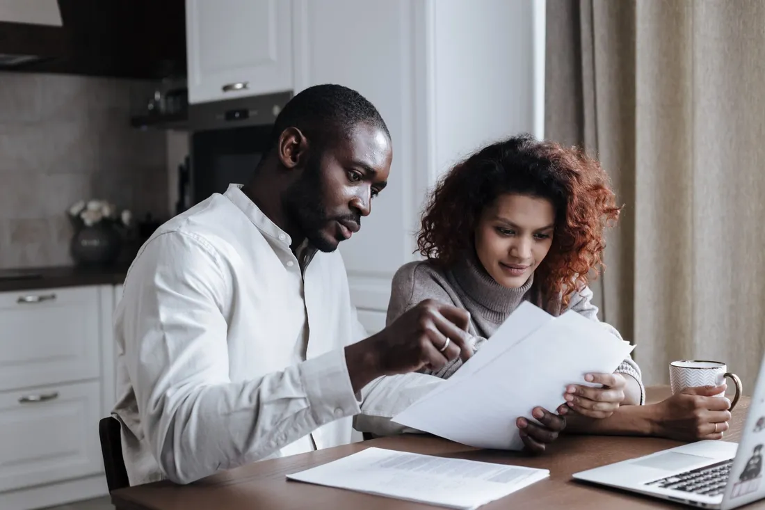 A couple comparing documents together at a kitchen table with a laptop