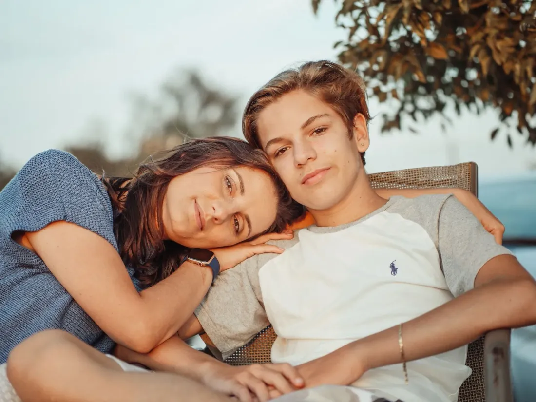A mother resting her head on her teenage son's shoulder outdoors