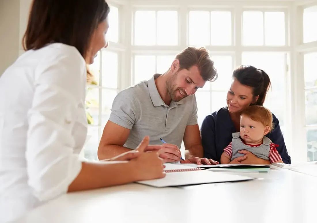 A father and mother with their baby filling in a form at a table beside a practitioner