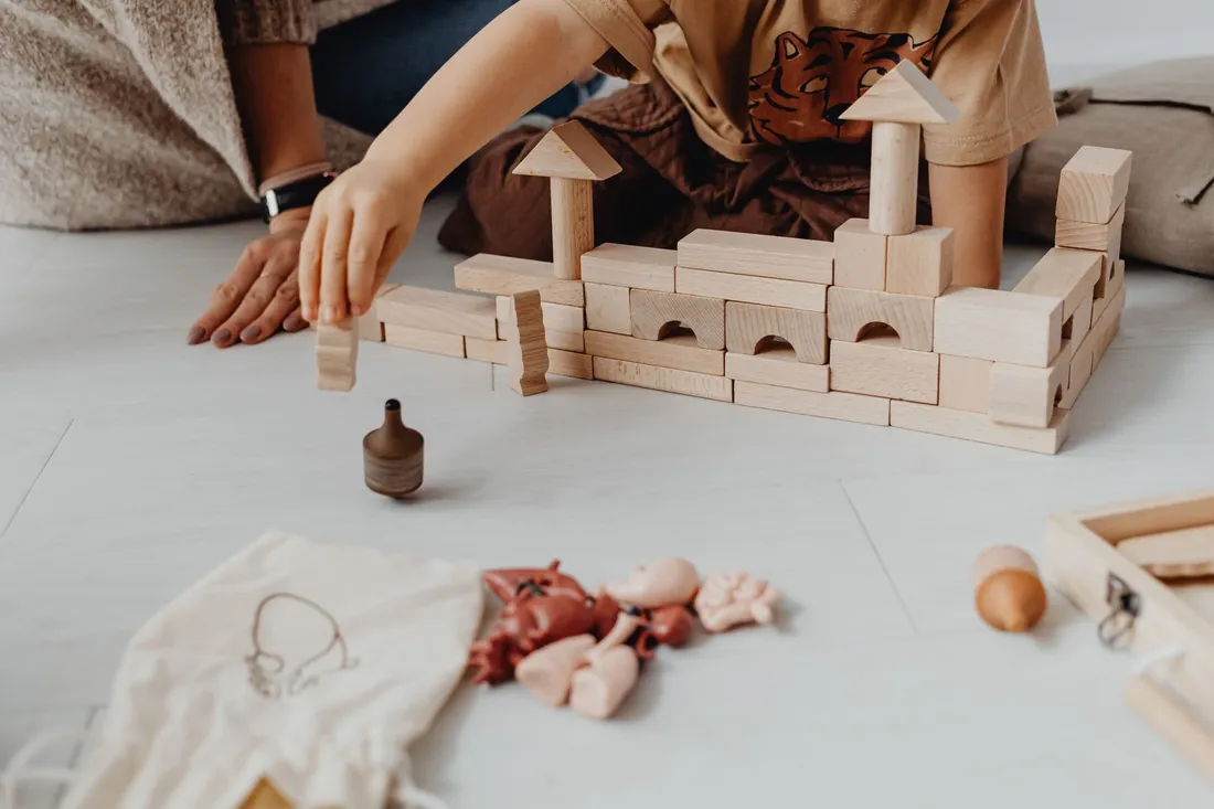 A child playing with wooden blocks and toys on a light floor