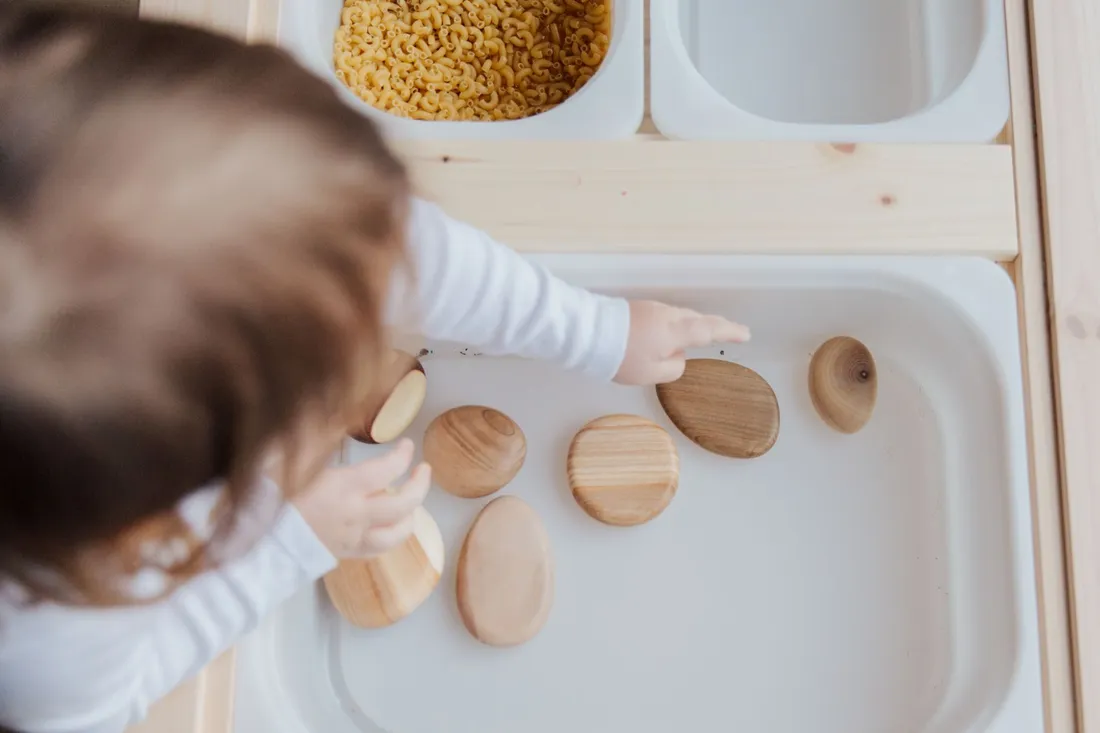 A young child picking smooth wooden stones from a tray in a sensory play activity
