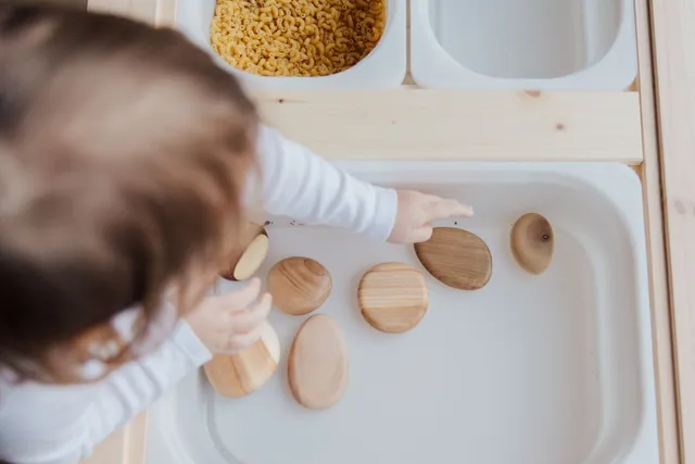 A young child picking smooth wooden stones from a tray in a sensory play activity