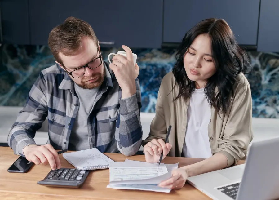 A couple going through paperwork with a calculator and laptop at the kitchen table
