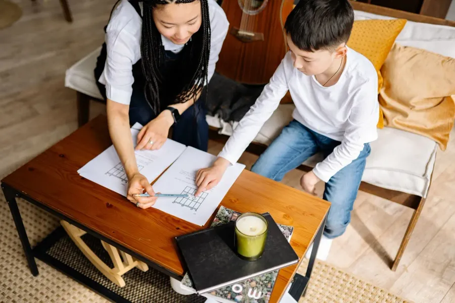 A woman and a boy working together over a sheet of paper at a table