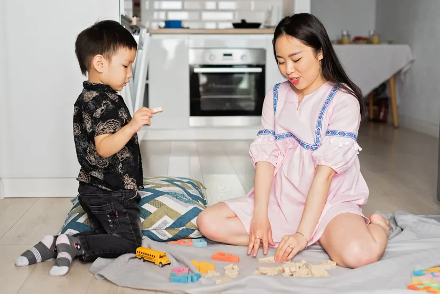 A mother and her young son playing with toys together on a rug at home